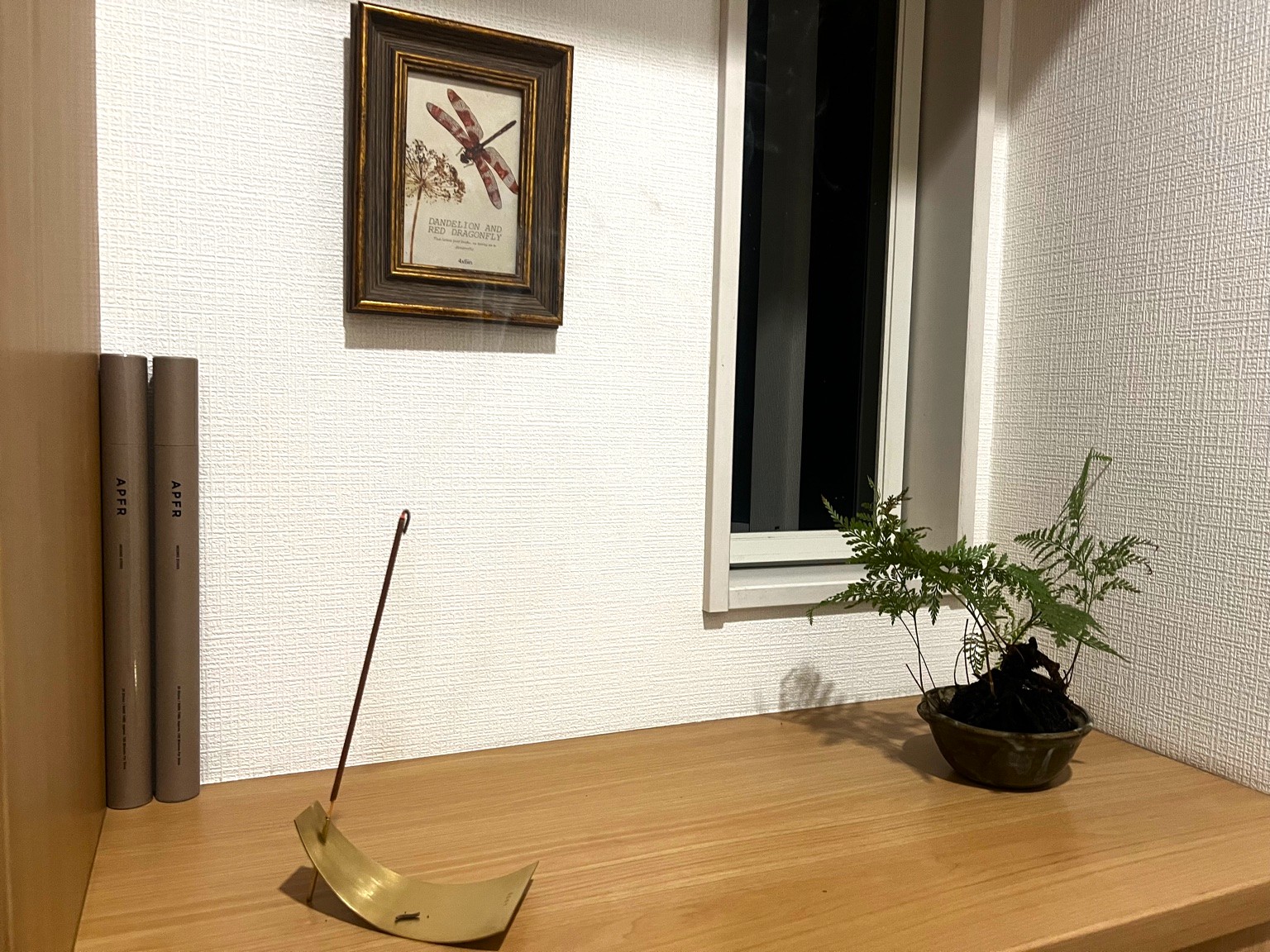 棚に置いた真鍮のお香立てとAPFRのお香、グリーン、壁のアートが並ぶ落ち着いたインテリアの写真。