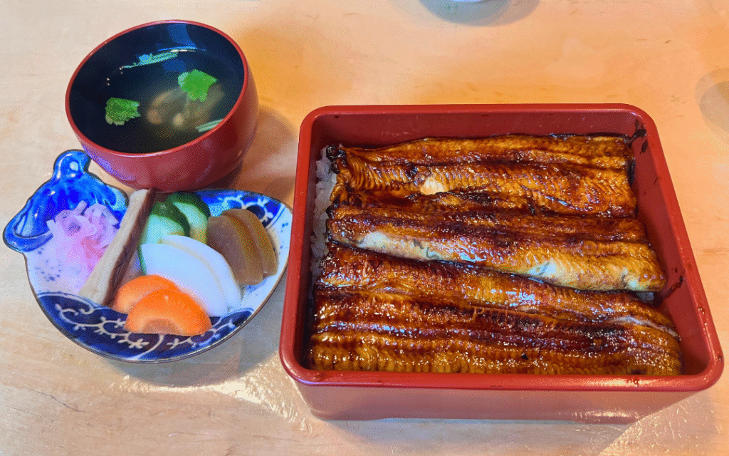 ふっくら肉厚に焼き上げた友栄のうな重。赤い重箱に美しく並ぶうなぎ。
